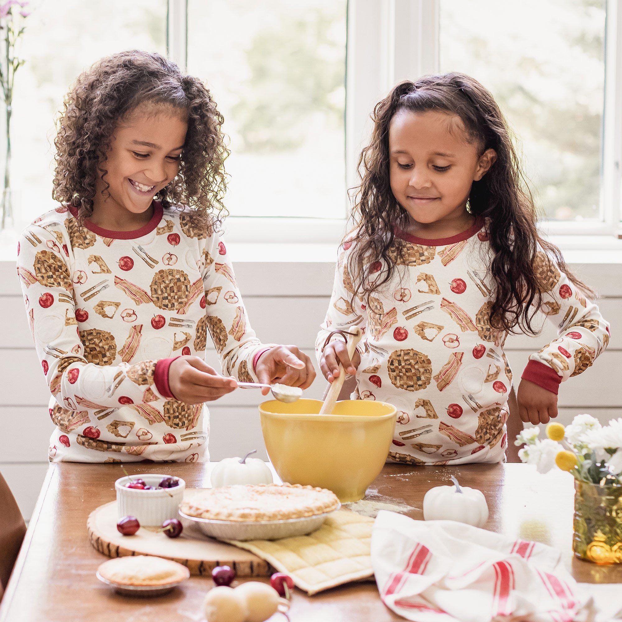 Two girls wearing organic cotton Burt's Bees Baby Thanksgiving pajamas and baking apple pie