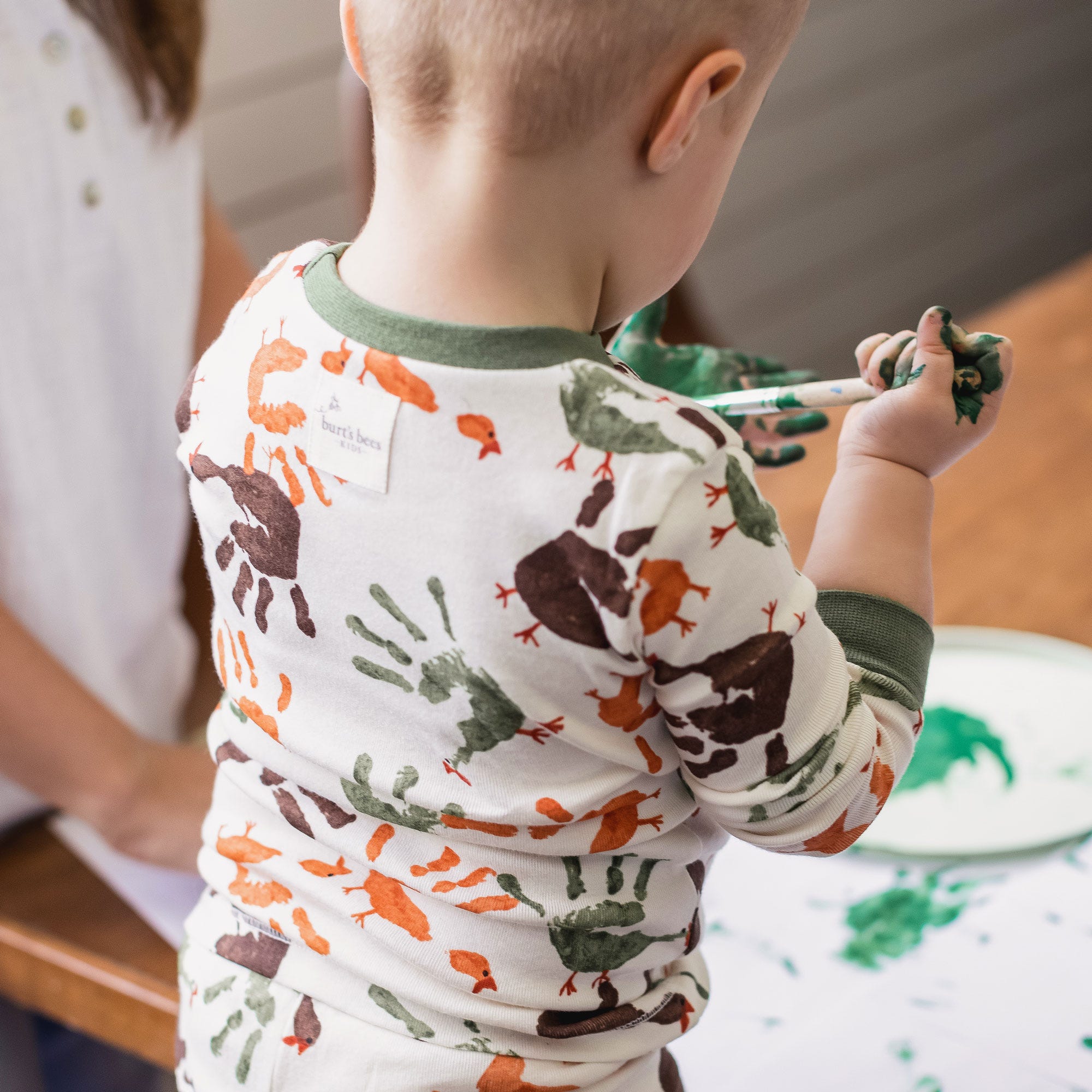 Toddler boy wearing organic cotton Burt's Bees Baby Thanksgiving pajamas and painting turkey hands